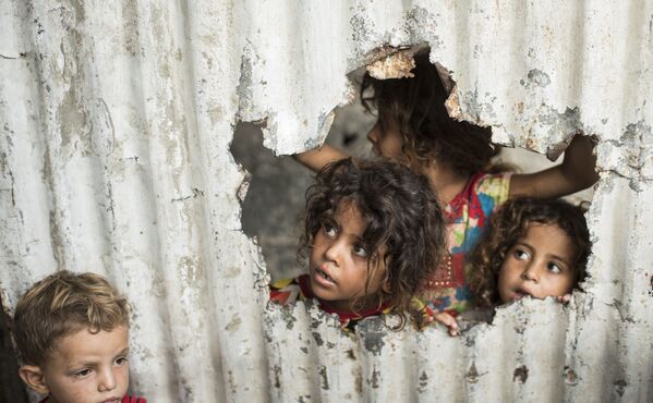 Палестинские дети смотрят через отверстие в заборе из листового металла в бедном районе города Газа - Sputnik Молдова