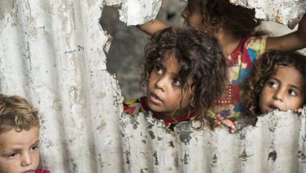 Палестинские дети смотрят через отверстие в заборе из листового металла в бедном районе города Газа - Sputnik Moldova-România