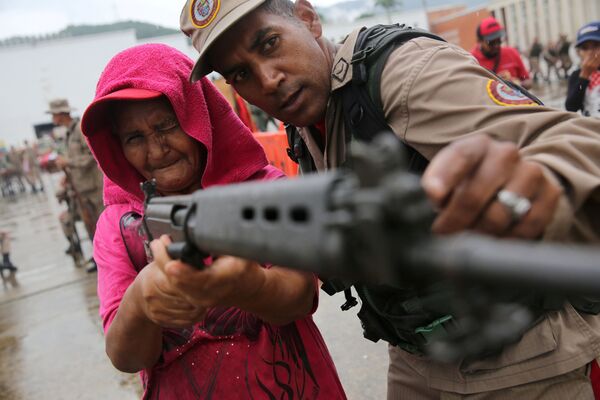 Полицейский Национальных боливарианских вооруженных сил учит женщину использовать винтовку во время военных учений в Каракасе - Sputnik Молдова