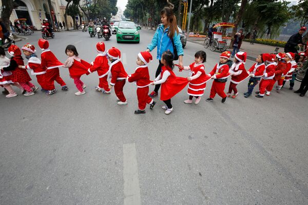 Дети в костюмах Санта-Клаусов переходят дорогу на улице в Ханое, Вьетнам - Sputnik Молдова