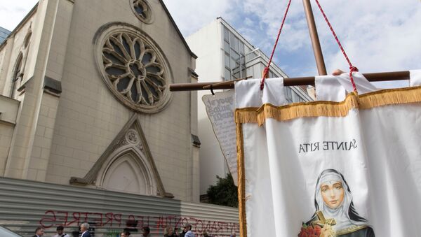 A person holds a banner picturing Sainte-Rita as other stand in front of barriers blocking the access to the sainte-Rita church in Paris with an inscription on it which translates as In France, priests are killed and churchs are demolished, on August 3, 2016 - Sputnik Moldova-România