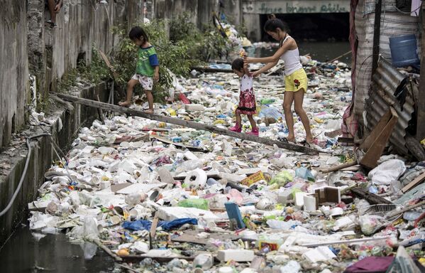 Жители дома проходят по деревянной дощечке через кучи мусора в Маниле, Филиппины - Sputnik Молдова