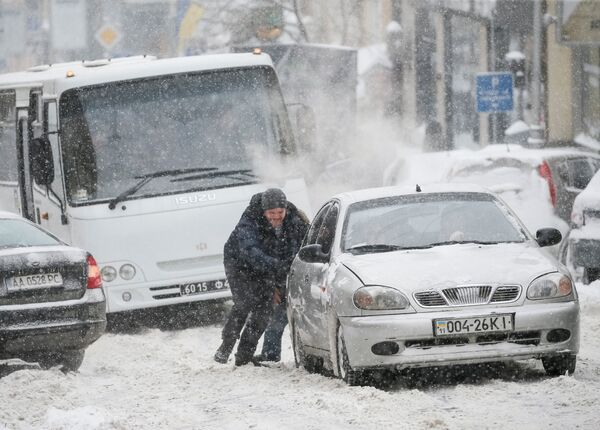 Человек подталкивает машину, попавшую в снег на улице в центре Киева, Украина - Sputnik Молдова