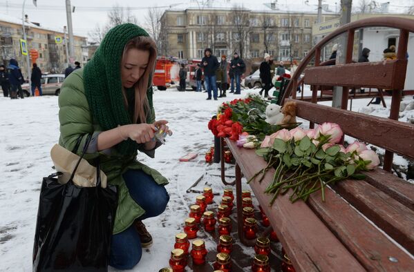 Женщина зажигает свечу возле здания торгового центра Зимняя вишня в Кемерово, где произошел пожар. - Sputnik Молдова