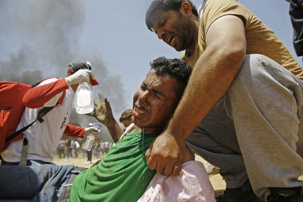 Палестинец помогает раненому демонстранту во время столкновений с израильскими военными в районе границы между Израилем и сектором Газа - Sputnik Moldova-România