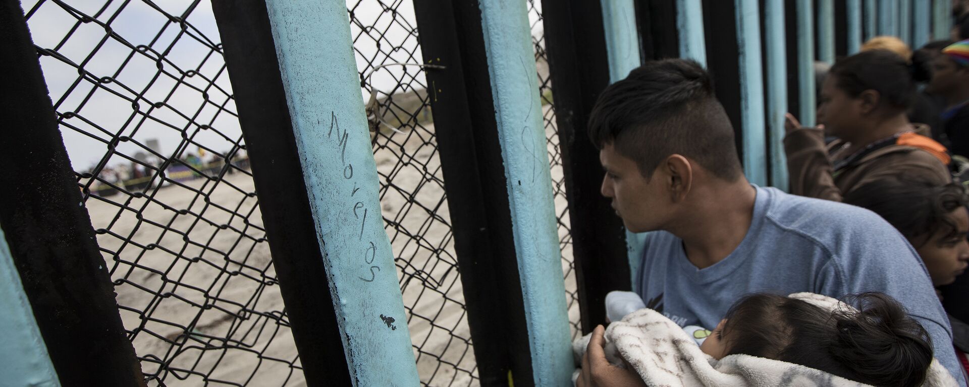 In this April 29, 2018 file photo, a member of the Central American migrant caravan, holding a child, looks through the border wall toward a group of people gathered on the U.S. side, as he stands on the beach where the border wall ends in the ocean, in Tijuana, Mexico, Sunday, April 29, 2018 - Sputnik Moldova, 1920, 07.07.2023