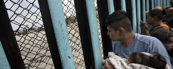 In this April 29, 2018 file photo, a member of the Central American migrant caravan, holding a child, looks through the border wall toward a group of people gathered on the U.S. side, as he stands on the beach where the border wall ends in the ocean, in Tijuana, Mexico, Sunday, April 29, 2018 - Sputnik Moldova-România