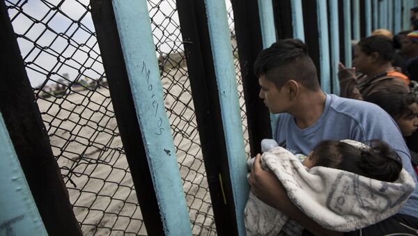In this April 29, 2018 file photo, a member of the Central American migrant caravan, holding a child, looks through the border wall toward a group of people gathered on the U.S. side, as he stands on the beach where the border wall ends in the ocean, in Tijuana, Mexico, Sunday, April 29, 2018 - Sputnik Moldova