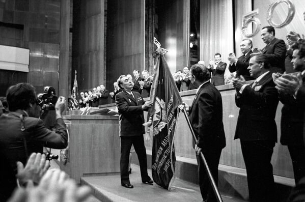 Secretarul general al PC al URSS L. I. Brejnev (la tribună) la festivitatea dedicată aniversării a 50-a a RSSM. L. I. Brejnev prinde Ordinul Revoluției din Octombrie de drapelul de stat al RSSM - Sputnik Moldova-România