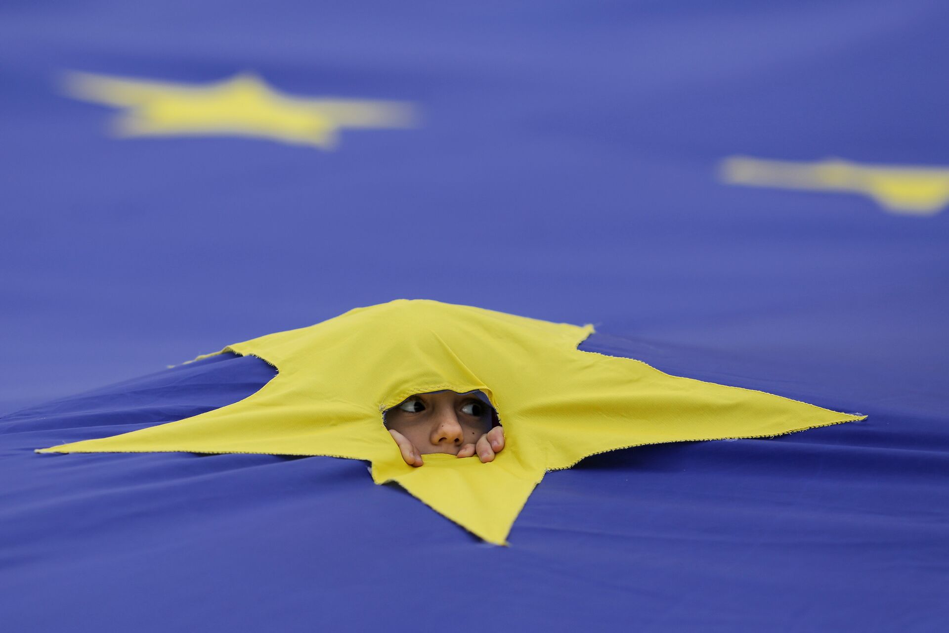Ребенок смотрит через разрез, сделанный на одной из звезд, которые составляют флаг Европейского Союза, во время митинга поддержки, организованного в честь 60-летия Европейского Союза в Риме, в центре Бухареста, Румыния - Sputnik Молдова, 1920, 30.07.2021