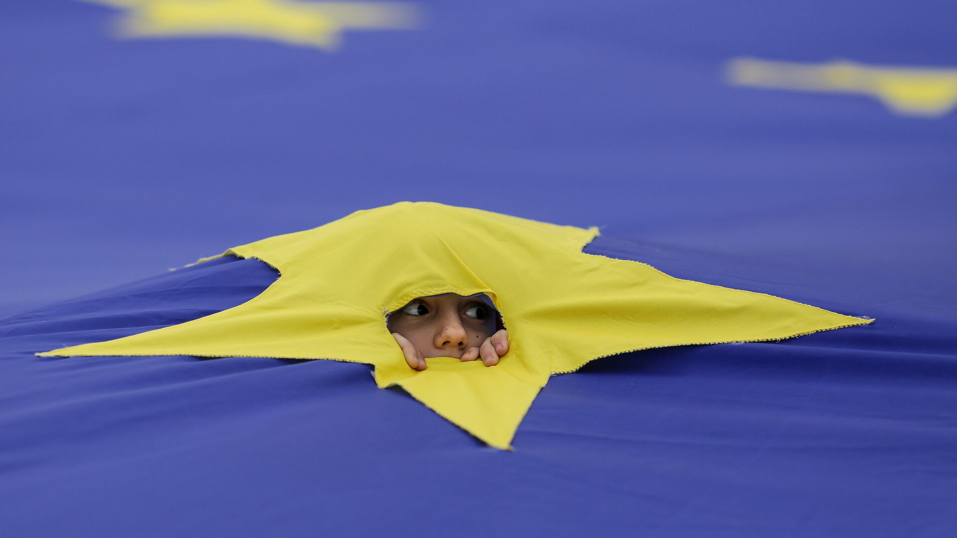 Ребенок смотрит через разрез, сделанный на одной из звезд, которые составляют флаг Европейского Союза, во время митинга поддержки, организованного в честь 60-летия Европейского Союза в Риме, в центре Бухареста, Румыния - Sputnik Moldova-România, 1920, 11.03.2022