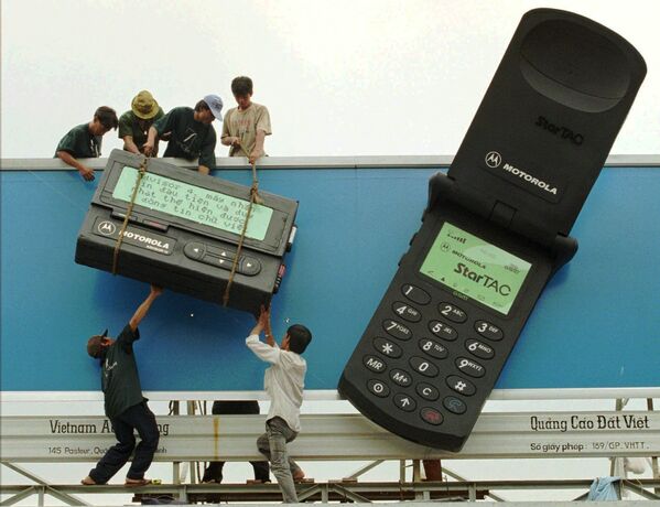 Рабочие размещают гигантский пейджер рядом с гигантским мобильным телефоном с рекламой телекоммуникационных продуктов Motorola в городе Хошимин, 1996 - Sputnik Молдова
