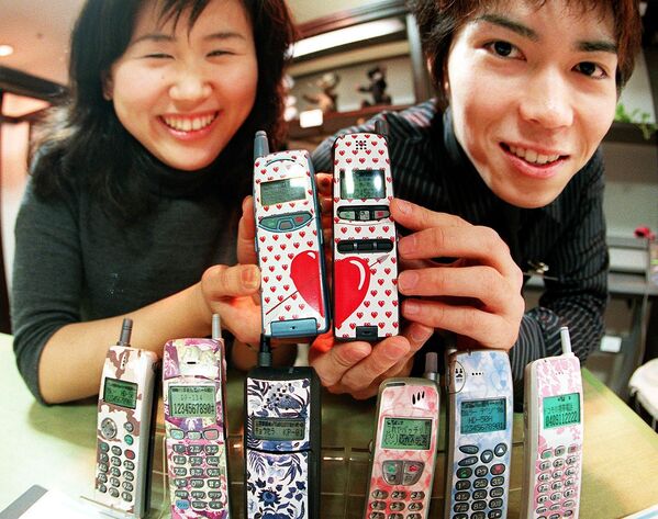 Молодая японская пара демонстрирует свои мобильные телефоны с дизайнерскими клеймами в универмаге Токи - Sputnik Молдова