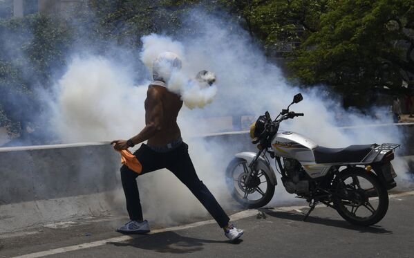 Протестующий кидает бутылку со слезоточивым газом во время столкновения с Национальной гвардией Венесуэлы в Альтамире, районе Каракаса - Sputnik Молдова