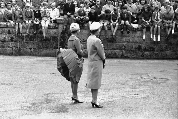 Ветер поднимает юбку принцессы Маргарет, пока они с королевой Елизаветой Второй ожидают прибытия президента США Дуайта Эйзенхауэра в замке Балморал, Шотландия - Sputnik Moldova-România