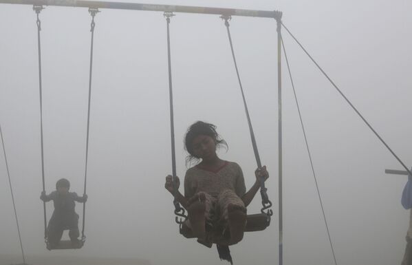 Дети катаются на качелях на детской площадке, окруженной смогом, в Лахоре - Sputnik Молдова