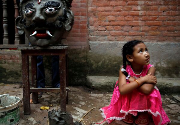 Девочка сидит рядом с головой демона Гхантакарны, прежде чем его сожгут на фестивале Гхантакарна, Непал - Sputnik Молдова
