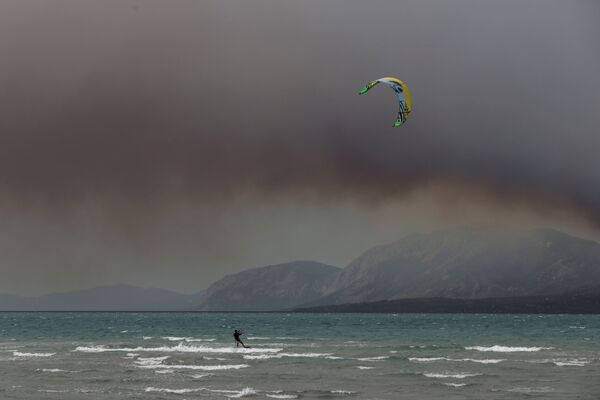 Un bărbat face kitesurfs în apropiere de țărmurile orașului Chalkida în timp ce fumul de la incendiul din insula Evia, Grecia, acoperă cerul. - Sputnik Moldova