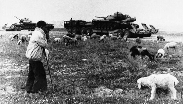 Молодой пастух наблюдает за танком, перевозящим грузовики возле разрушенного войной города Ахваз, Иран, 17 апреля 1981 года - Sputnik Moldova-România
