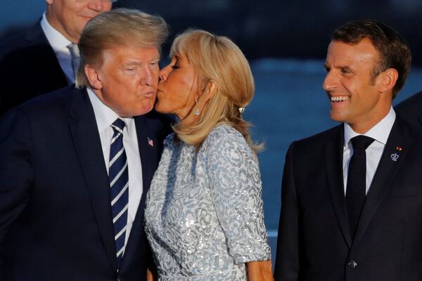 Președintele francez Emmanuel Macron se uită la soția sa, Brigitte Macron, în timp ce aceasta îl sărută pe președintele SUA, Donald Trump, în cadrul unei sesiuni de fotografie de familie cu invitați în timpul summitului G7 de la Biarritz, Franța, 25 august 2019. - Sputnik Moldova-România
