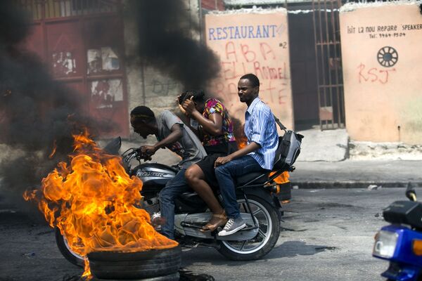 Мото-такси проезжающее мимо горящей шины в Порт-о-Пренсе, Гаити - Sputnik Молдова