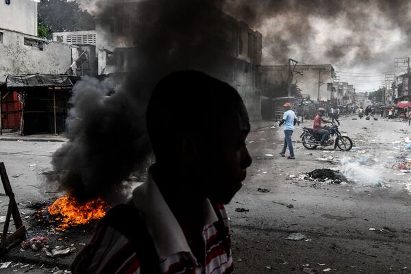 Мужчина, идущий мимо горящих шин во время протеста в Порт-о-Пренсе, Гаити - Sputnik Молдова
