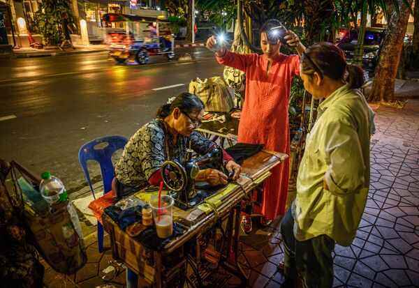 Женщина освещает мобильными телефонами рабочее место уличной швее в Бангкоке, Таиланд  - Sputnik Молдова