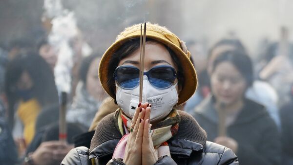 Женщина в маске и солнцезащитных очках во время молитвы в первый день Нового года в Пекине - Sputnik Молдова