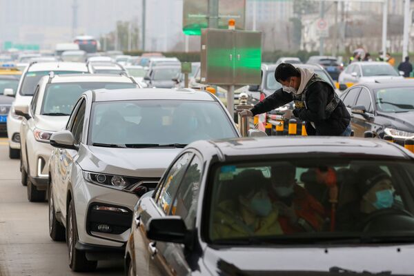 Сотрудник группы по санитарии и профилактике эпидемий проверяет температуру тела пассажира в автомобиле на стоянке в Ухане, Китай - Sputnik Молдова