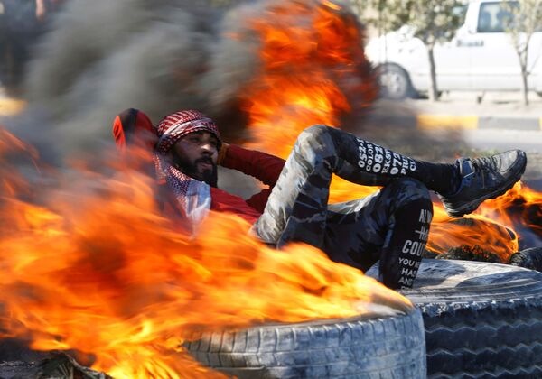 Демонстрант среди горящих шин, блокирующих дорогу во время антиправительственных акций протеста в Наджафе, Ирак - Sputnik Молдова