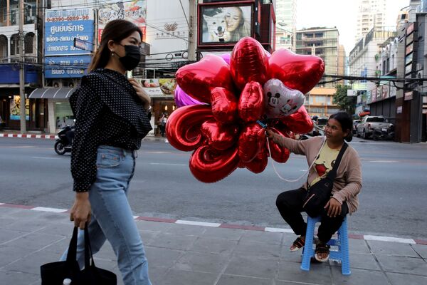 Женщина в медицинской маске проходит мимо продавщицы воздушных шаров накануне Дня святого Валентина в Бангкоке, Таиланд  - Sputnik Молдова