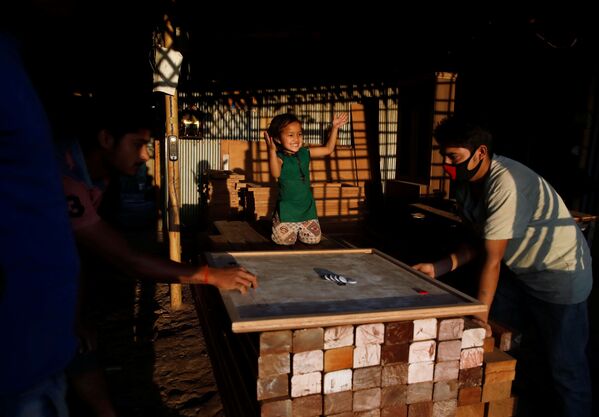 Маленькая девочка болеет за отца, играющего в карром в мебельной мастерской в Лалитпур, Непал - Sputnik Молдова