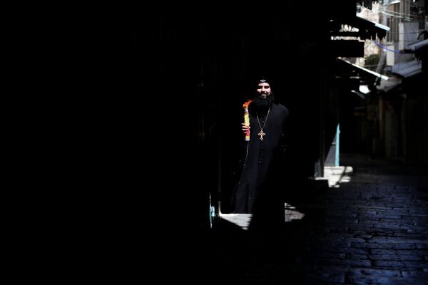 Православный христианский священнослужитель держит свечи в руках после церемонии Священного Огня рядом с Церковью Гроба Господня в Старом городе Иерусалима в разгар вспышки коронавирусной болезни  - Sputnik Молдова