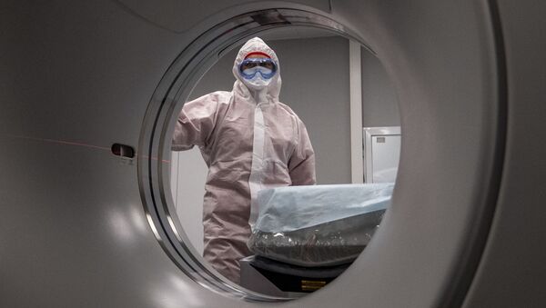Медицинский работник в защитном снаряжении стоит рядом со сканером компьютерной томографии  - Sputnik Moldova