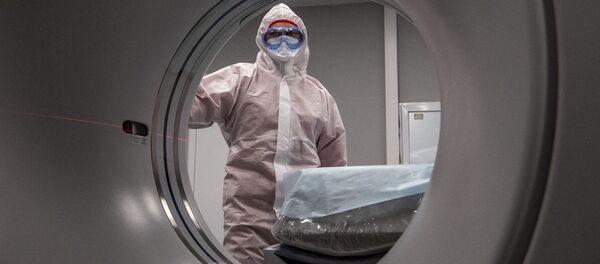 Медицинский работник в защитном снаряжении стоит рядом со сканером компьютерной томографии  - Sputnik Moldova