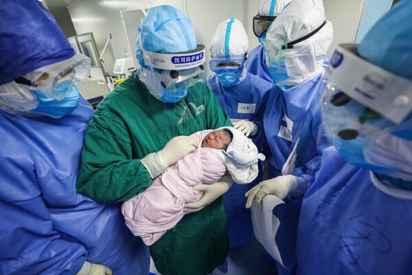 Медицинский работник в защитном костюме держит на руках новорожденного в отделении для инфицированных коронавирусом беременных в больнице Уханя, Китай - Sputnik Moldova-România