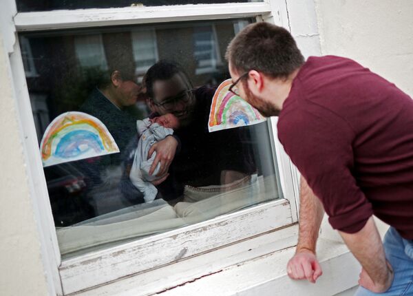 Мужчина смотрит через окно на свою новорожденную племянницу в период пандемии коронавируса в Великобритании - Sputnik Moldova-România
