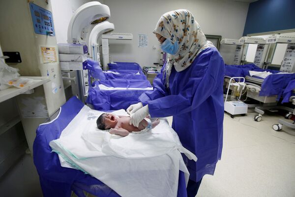 Медсестра в защитной маске и перчатках ухаживает за новорожденным в роддоме в Наджафе, Ирак - Sputnik Moldova-România