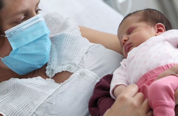 Зараженная коронавирусом женщина в защитной маске с новорожденной дочерью в больнице Брюсселя, Бельгия - Sputnik Moldova