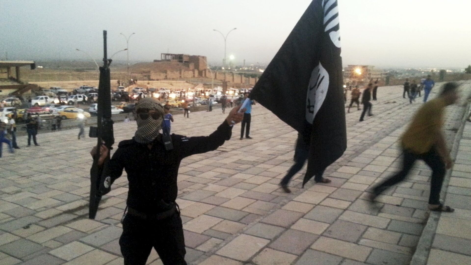 A fighter of Daesh holds an ISIL flag and a weapon on a street in the city of Mosul, Iraq, in this June 23, 2014. - Sputnik Moldova-România, 1920, 21.08.2021