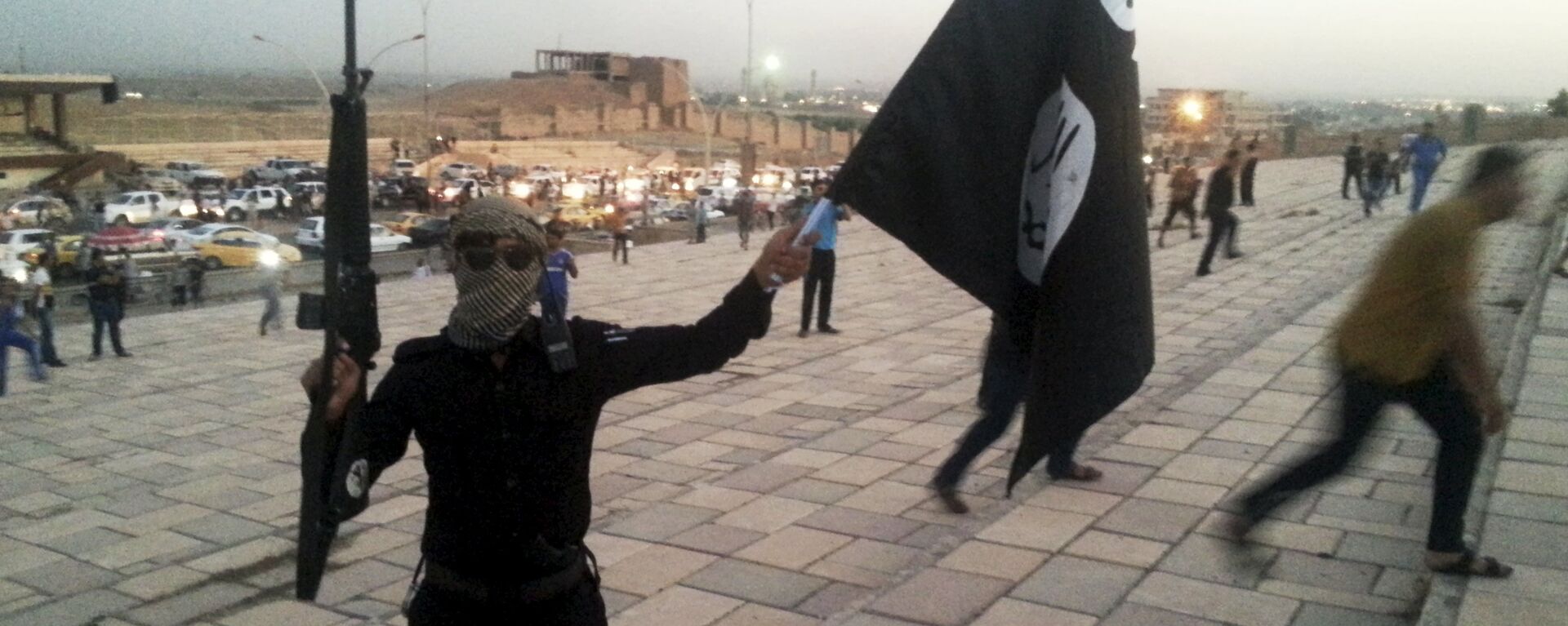 A fighter of Daesh holds an ISIL flag and a weapon on a street in the city of Mosul, Iraq, in this June 23, 2014. - Sputnik Moldova-România, 1920, 21.08.2021