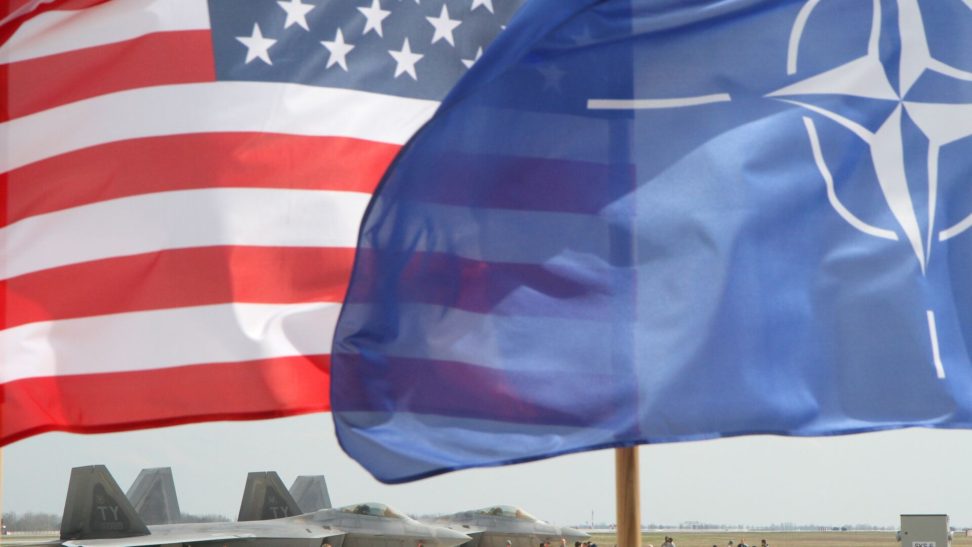 The US and The NATO flag flie in front of two US Air Force F-22 Raptor fighter aircrafts at the Air Base of the Lithuanian Armed Forces in Šiauliai, Lithuania, on April 27, 2016.  - Sputnik Moldova-România, 1920, 03.06.2021