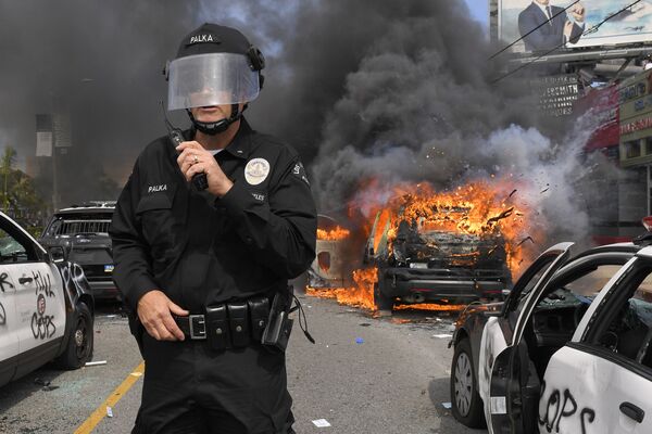 Полицейский Лос-Анджелеса на фоне горящей машины во время протестов  - Sputnik Moldova