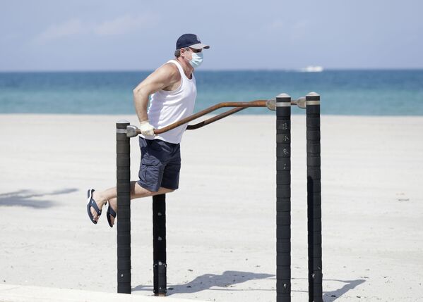 Мужчина в защитной маске во время выполнения упражнений на турнике на пляже в Голливуде, США - Sputnik Молдова