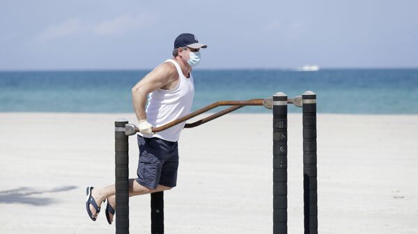 Мужчина в защитной маске во время выполнения упражнений на турнике на пляже в Голливуде, США - Sputnik Moldova