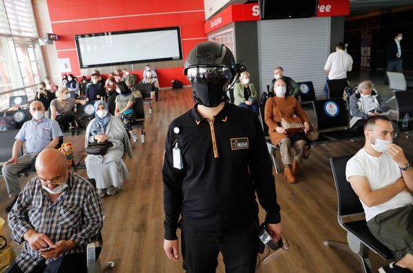 Сотрудник службы безопасности в тепловизионном шлеме следит за пассажирами, ожидающими посадки на рейс в аэропорту Стамбула - Sputnik Молдова