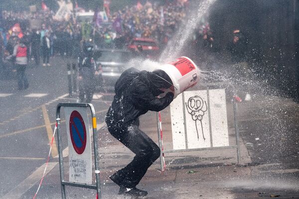 Протестующий прикрывается ведром от удара водяной пушкой, которую полицейские используют для разгона акции протеста медработников в Нанте, Франция - Sputnik Молдова
