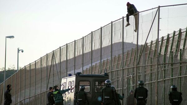 An African migrant sits atop a border fence, above Spanish Civil Guard officers, during an attempt to cross into Spanish territories, between Morocco and Spain's north African enclave of Melilla December 19, 2014. - Sputnik Moldova-România