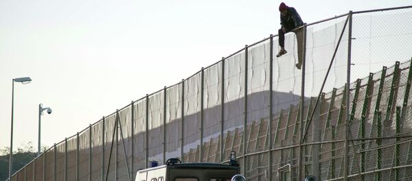 An African migrant sits atop a border fence, above Spanish Civil Guard officers, during an attempt to cross into Spanish territories, between Morocco and Spain's north African enclave of Melilla December 19, 2014. - Sputnik Moldova-România