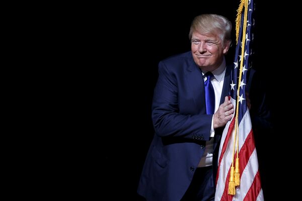 Candidatul republican la președinția SUA, Donald Trump, îmbrățișeaza un steag american pe scena de la o reuniune în campania primară din Derry, New Hampshire, 19 august 2015. - Sputnik Moldova